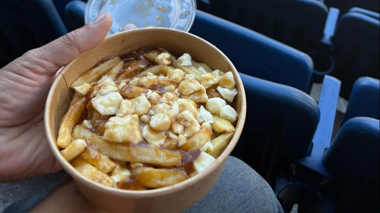 A fan in the stands, holding a bowl of poutine