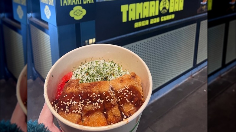 A hand holding a bowl of curry in front of a food stand