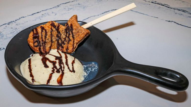 A serving skillet with a fish waffle on a stick and scoop of ice cream