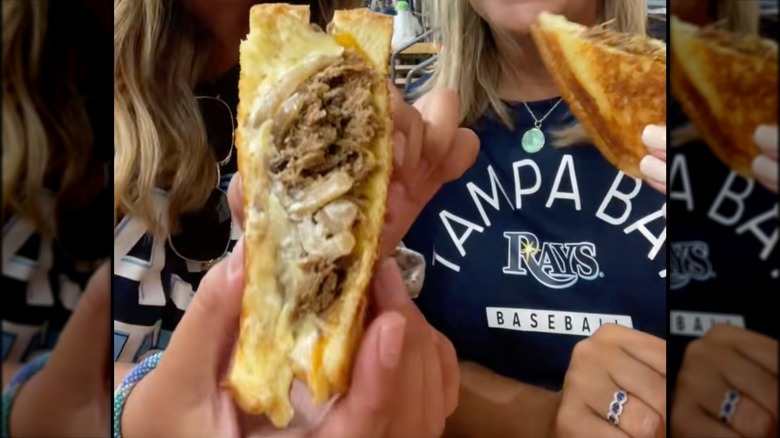 Two fans holding short rib grilled cheese sandwiches