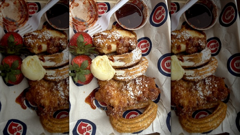 A tray with fried chicken and churros, with a dip and strawberries