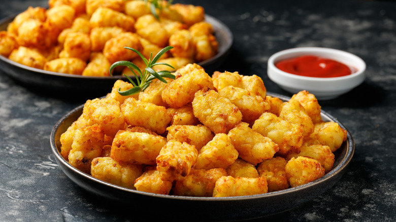 Two bowls of tater tots next to a small dish of ketchup
