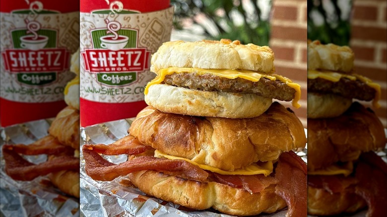 Biscuit sausage sandwich stacked on top of croissant bacon sandwich with Sheetz coffee cup behind