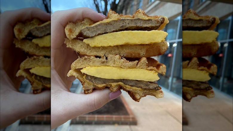 Hand holding a waffle breakfast sandwich cut in half and stacked