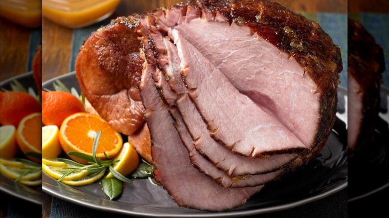 a spiral-cut ham on a platter garnished with orange halves and rosemany sprigs