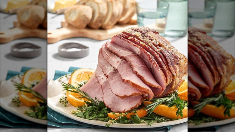 a spiral-sliced ham on a platter garnished with oranges and a rosemary