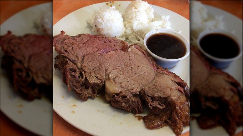 Prime rib with au jus and rice on a white plate against a wooden background