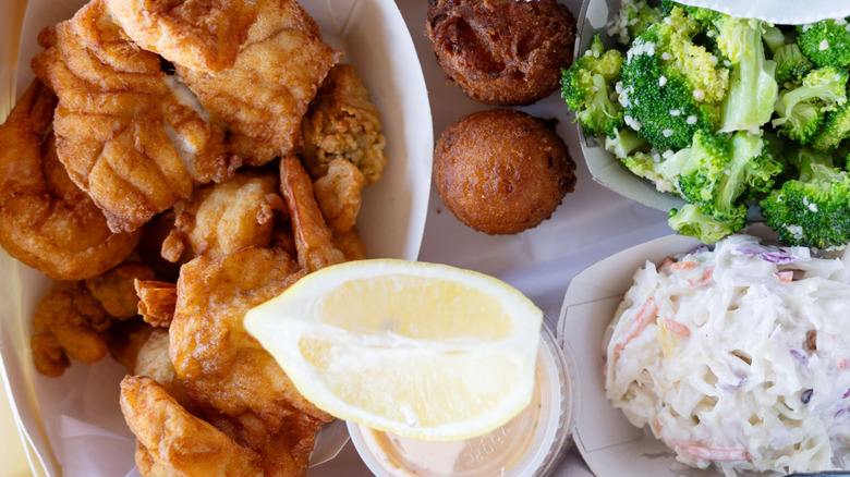 Fried mullet with hushpuppies, broccoli, and coleslaw against a white background