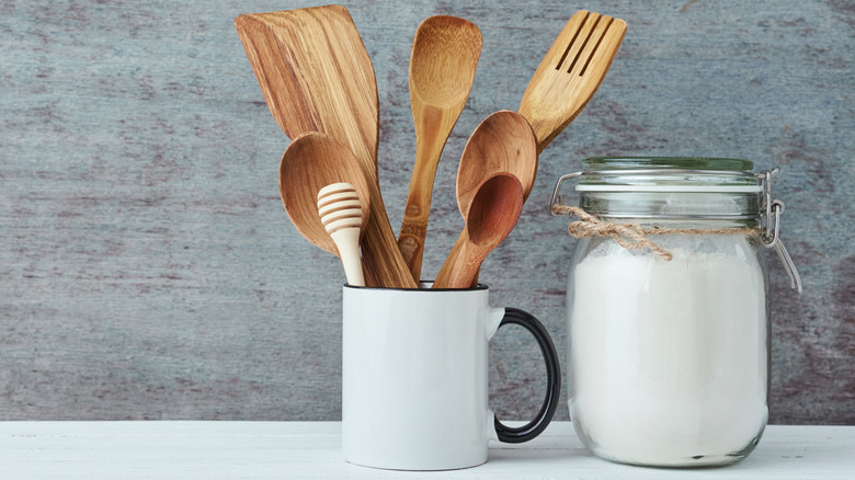 Kitchen utensils in a ceramic cup, next to a jar of flour