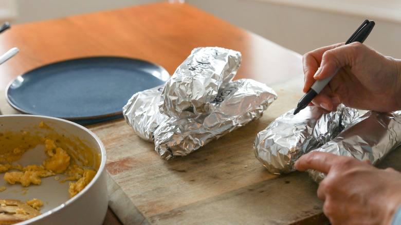 A person writes labels on foil-wrapped breakfast burritos