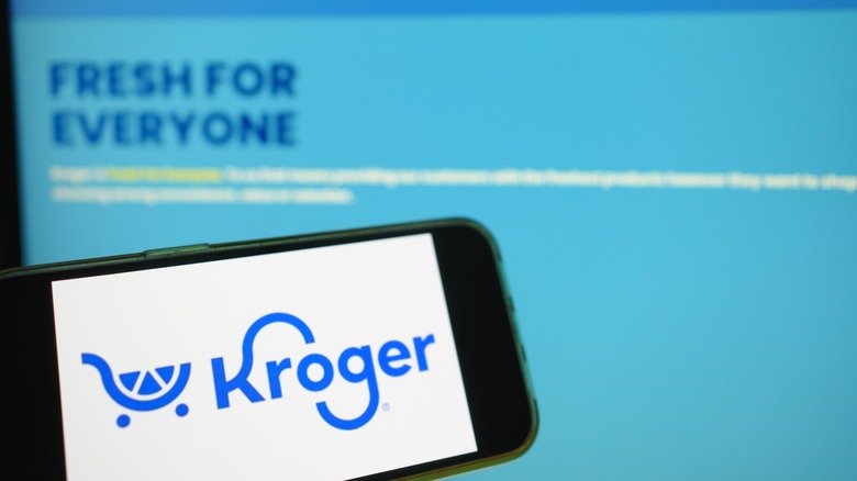 The Kroger logo is displayed on a smartphone, with the words "Fresh For Everyone" blurred in the background