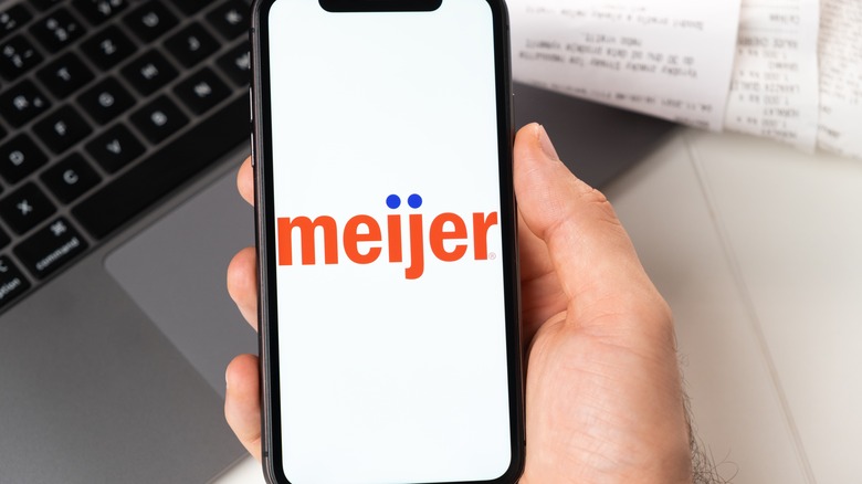A hand holds a phone with the Meijer logo on it