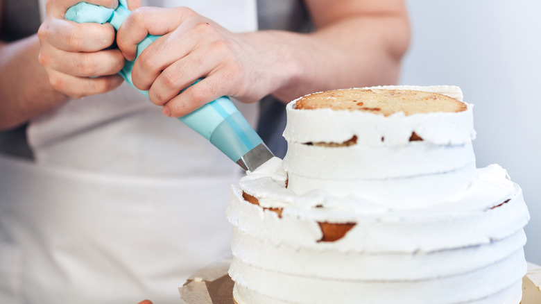 person frosting a cake with white icing