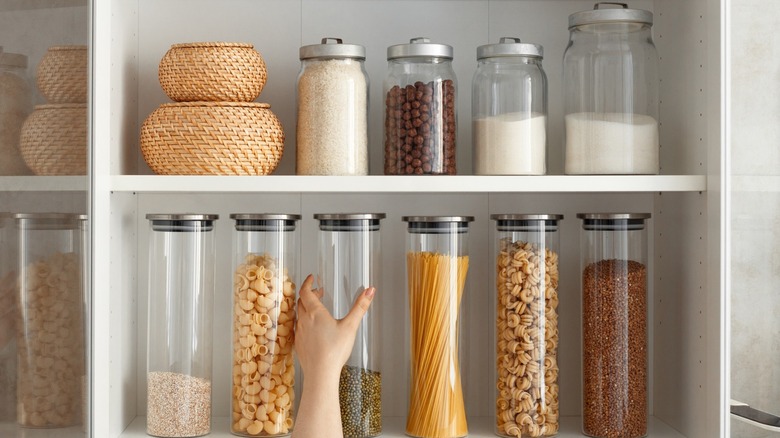A hand reaching up to a glass jar on shelf