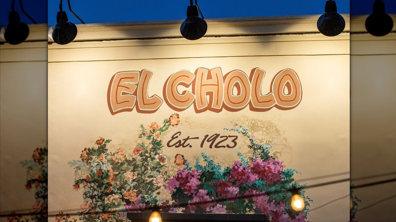 Logo for El Cholo restaurant painted on a wall, with "Est. 1923" and 2 flower bushes