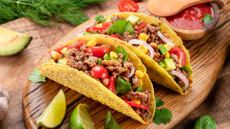 Beef tacos with sliced limes, herbs, and sauce on a wood cutting board