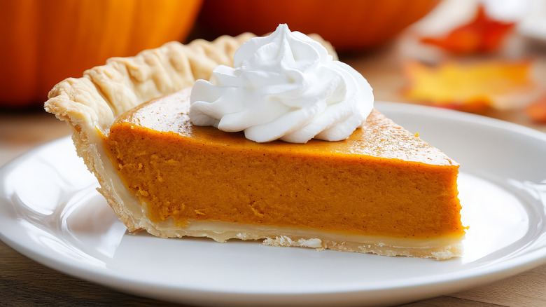 A perfect slice of pumpkin pie with whipped cream on top of it.