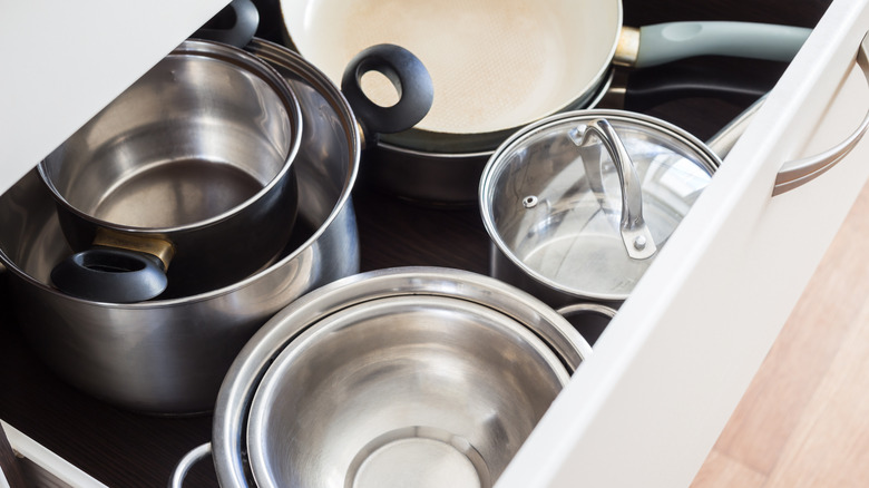 A large open cabinet drawer with many loose pots and pans