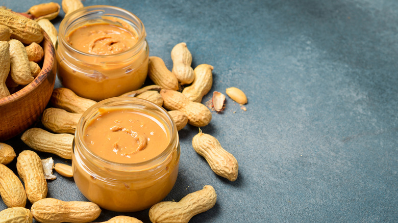 Two open jars of peanut butter, shot from above, with peanuts in shells beside them