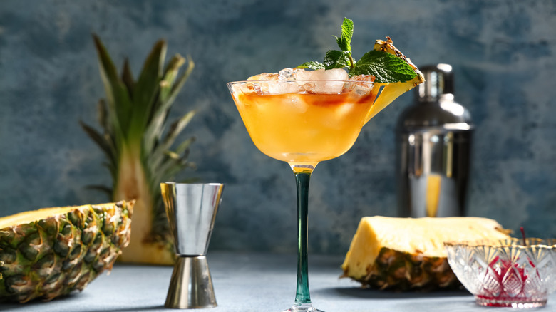 A mai tai in a martini glass garnished with pineapple and mint leaves