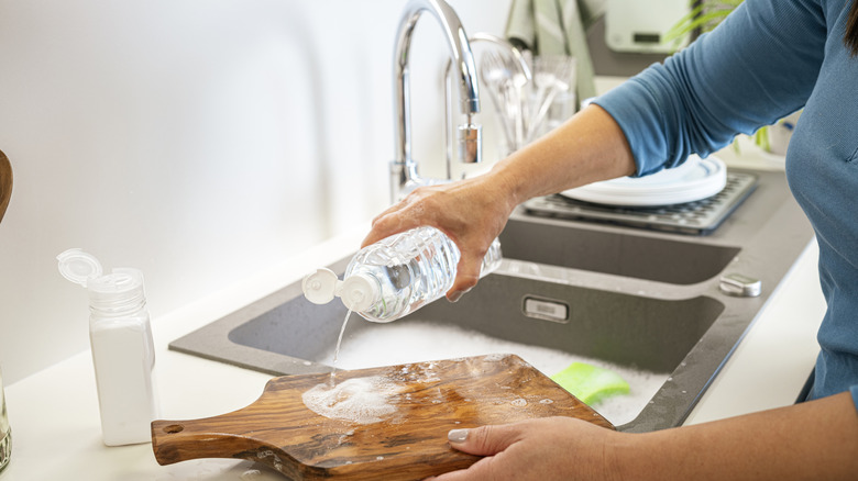 Woman washing a wooden cutting board by the sink