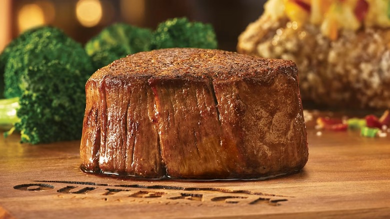 A cooked 6 ounce filet mignon on a wood cutting board with the Outback Steakhouse logo