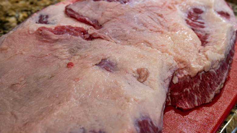 The fatty exterior of a raw brisket on a red surface.