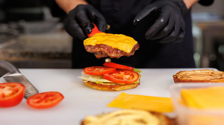 A cook assembling a cheeseburger in a professional kitchen
