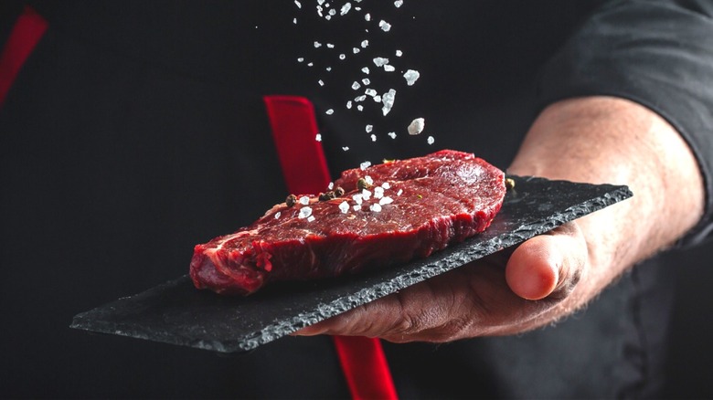 hand salting a steak on stone plate