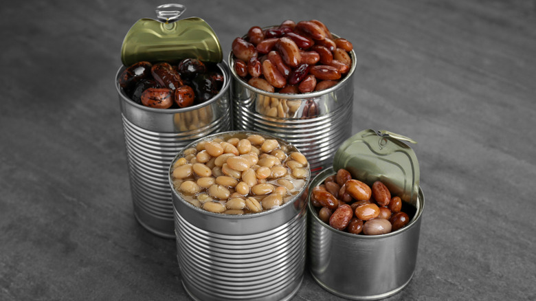 Four opened cans of beans brimming with the liquid and contents of each can