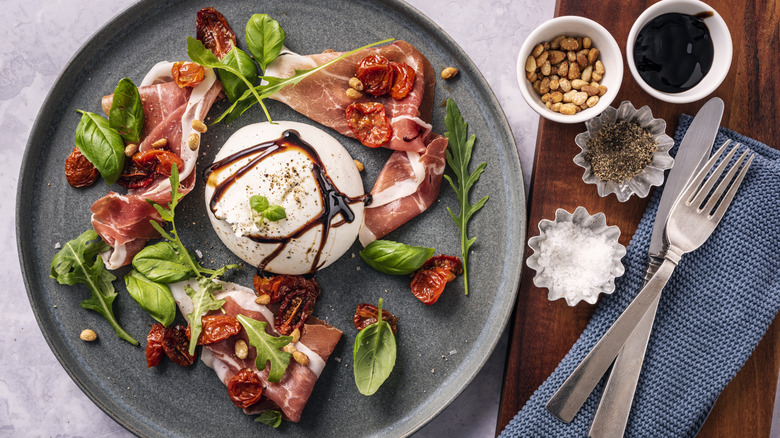 A gourmet salad, with cured ham, a ball of burrata, and salad leaves, with a balsamic glaze