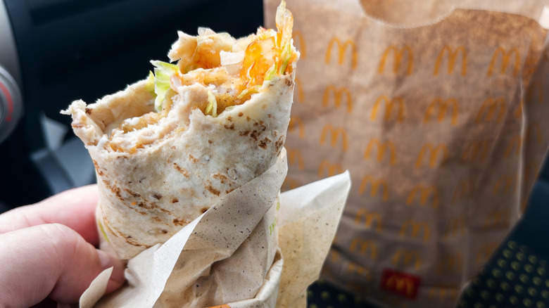 A hand holds a McDonald's breakfast burrito, with a bite taken out of it, in a car