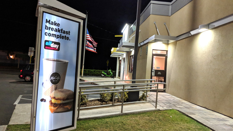 The exterior of a McDonald's restaurant is seen in darkness, with an illuminated sign outside advertising all-day breakfast