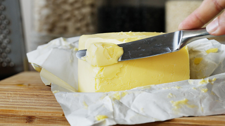 A knife slices a small piece of butter from a stick