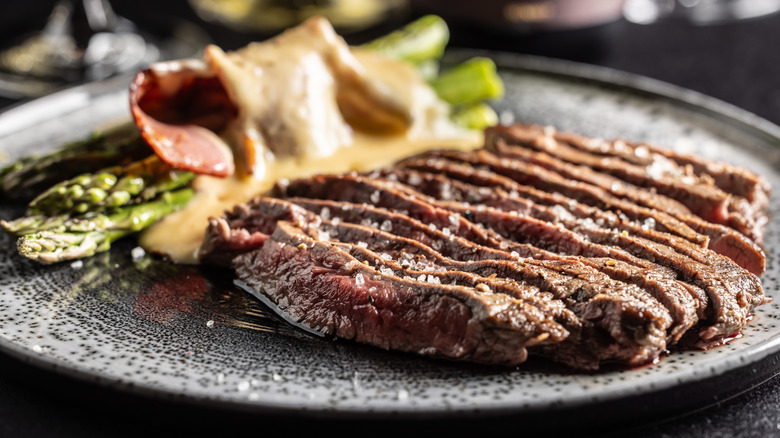 Sliced flank steak arranged on a plate with asparagus covered in a sauce.