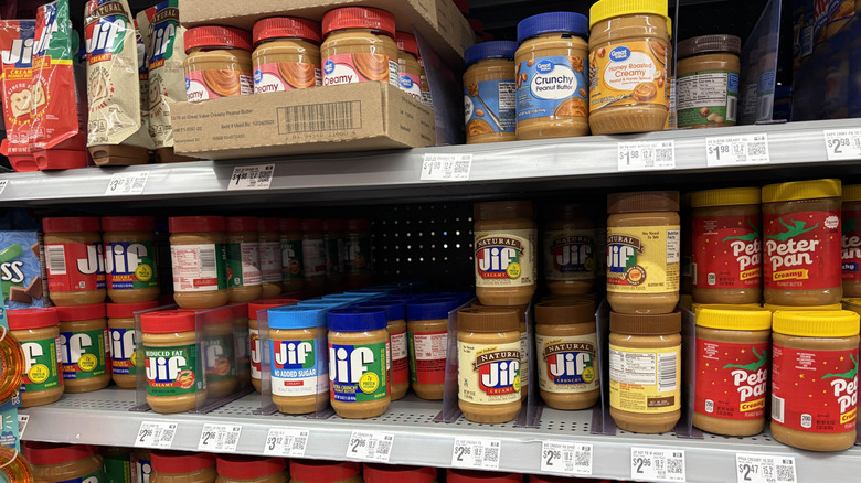 Rows of different peanut butter brands on a grocery shelf, including Great Value and Peter Pan peanut butters