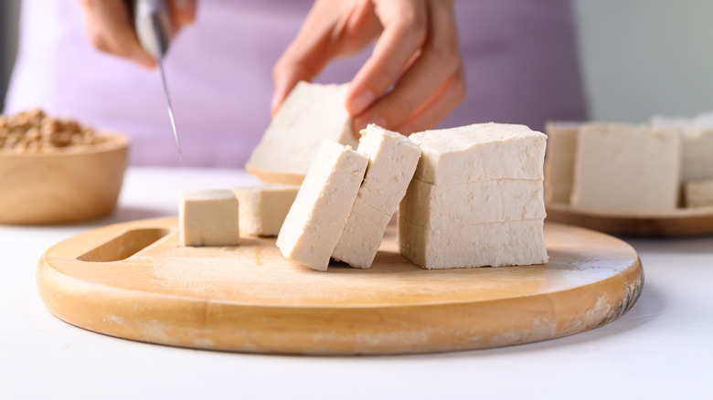 Hand preparing tofu on wood board
