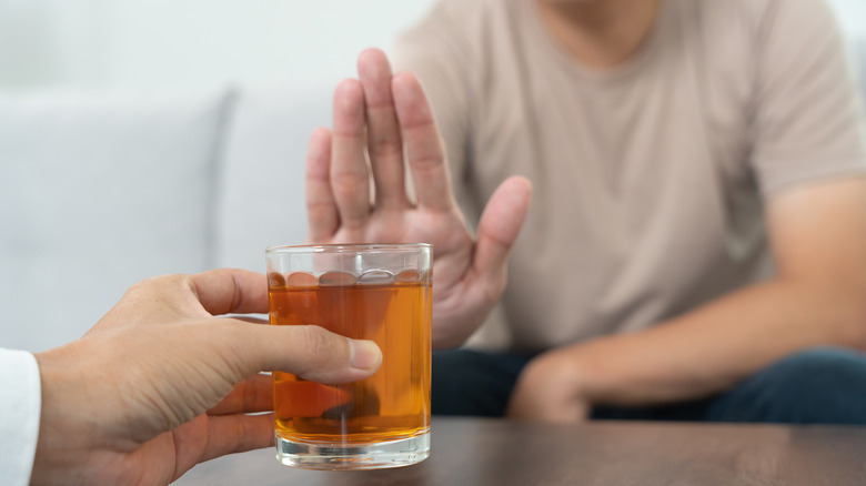 Person with a hand up refusing a glass of alcohol.
