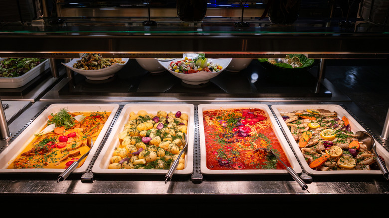 Four warmed trays of food on a stainless steel buffet line