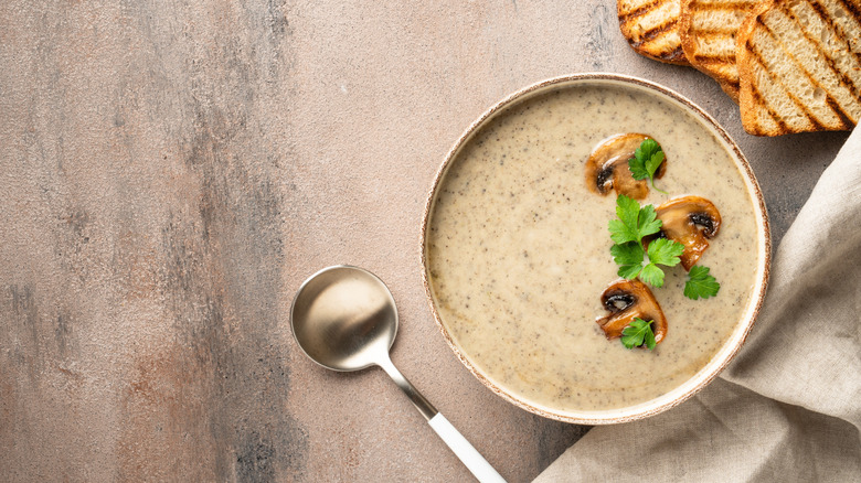A bowl of mushroom soup next to a spoon and toasted bread