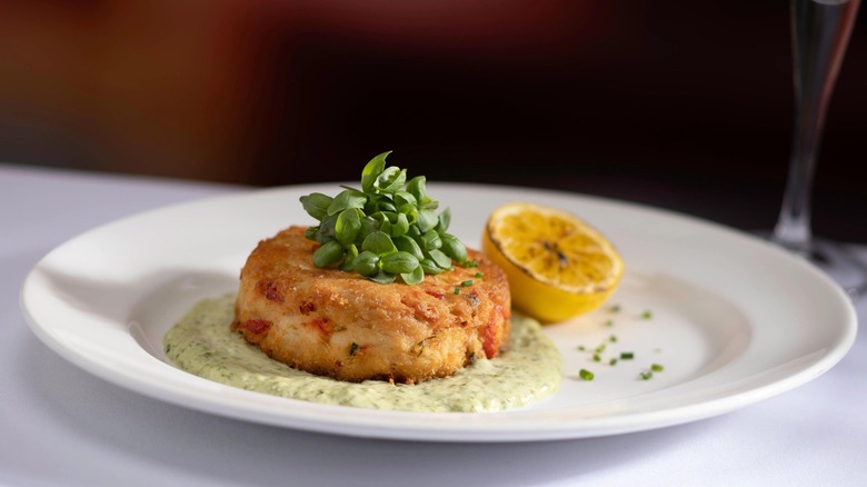 A crab cake is served atop lemon basil aioli on a white plate at The Capital Grille