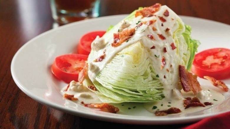 Close up of a wedge salad with dressing, tomato, and bacon on a white plate at The Capital Grille