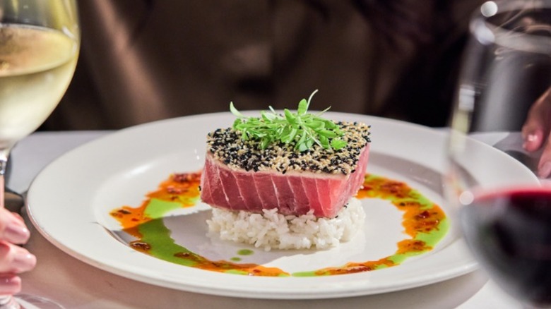 A seared tuna encrusted with sesame seeds sits atop rice on a white plate at The Capital Grille