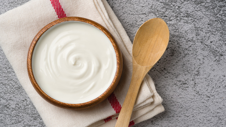 Yogurt in a bowl on a folded cloth with a wooden spoon.