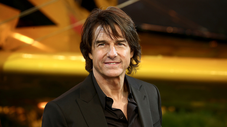 Tom Cruise wearing a black suit in front of and orange/yellow plane.