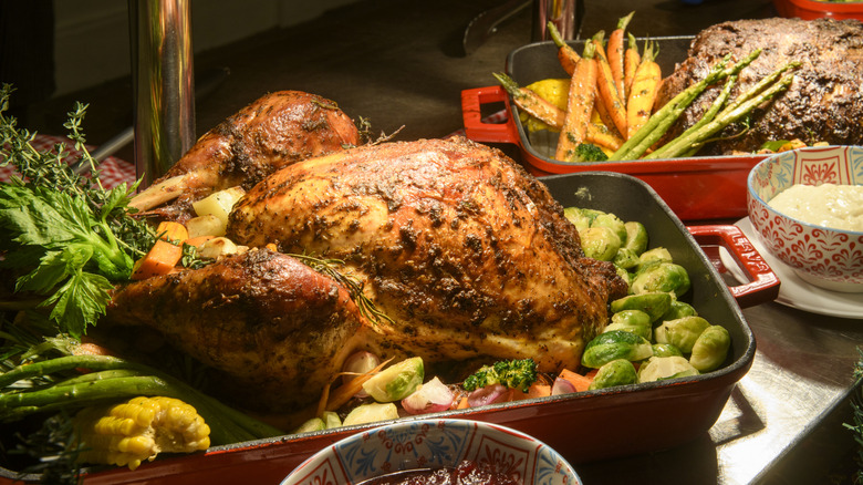 Roast chicken and vegetables in a red roasting pan, another cut of meat and carrots are behind in a second red pan