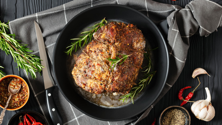 Roast pork in a cast iron skillet, with spices and herbs scattered nearby