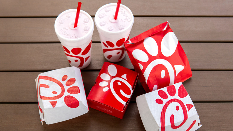 An assortment of Chick-fil-A items and drinks in red and white bags and boxes arranged on a table