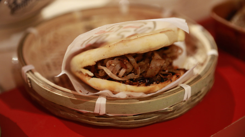 A juicy roujiamo served on a traditional bamboo plate