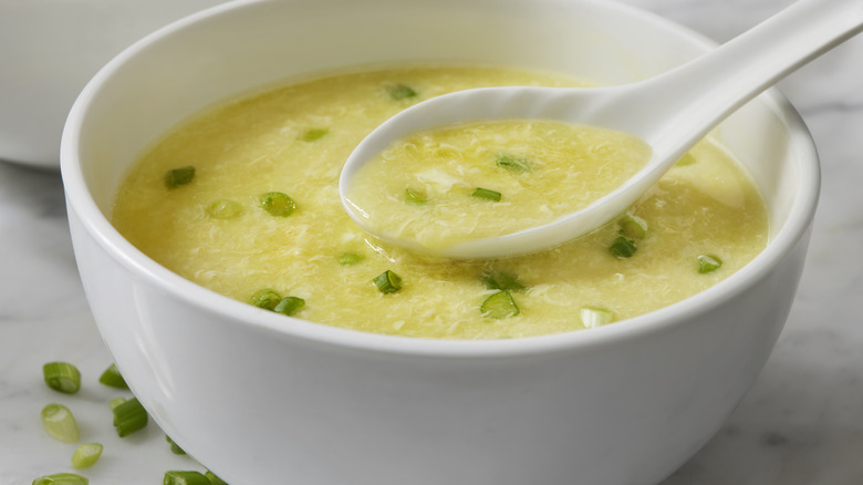 spoon scooping up egg drop soup with scallions from a bowl